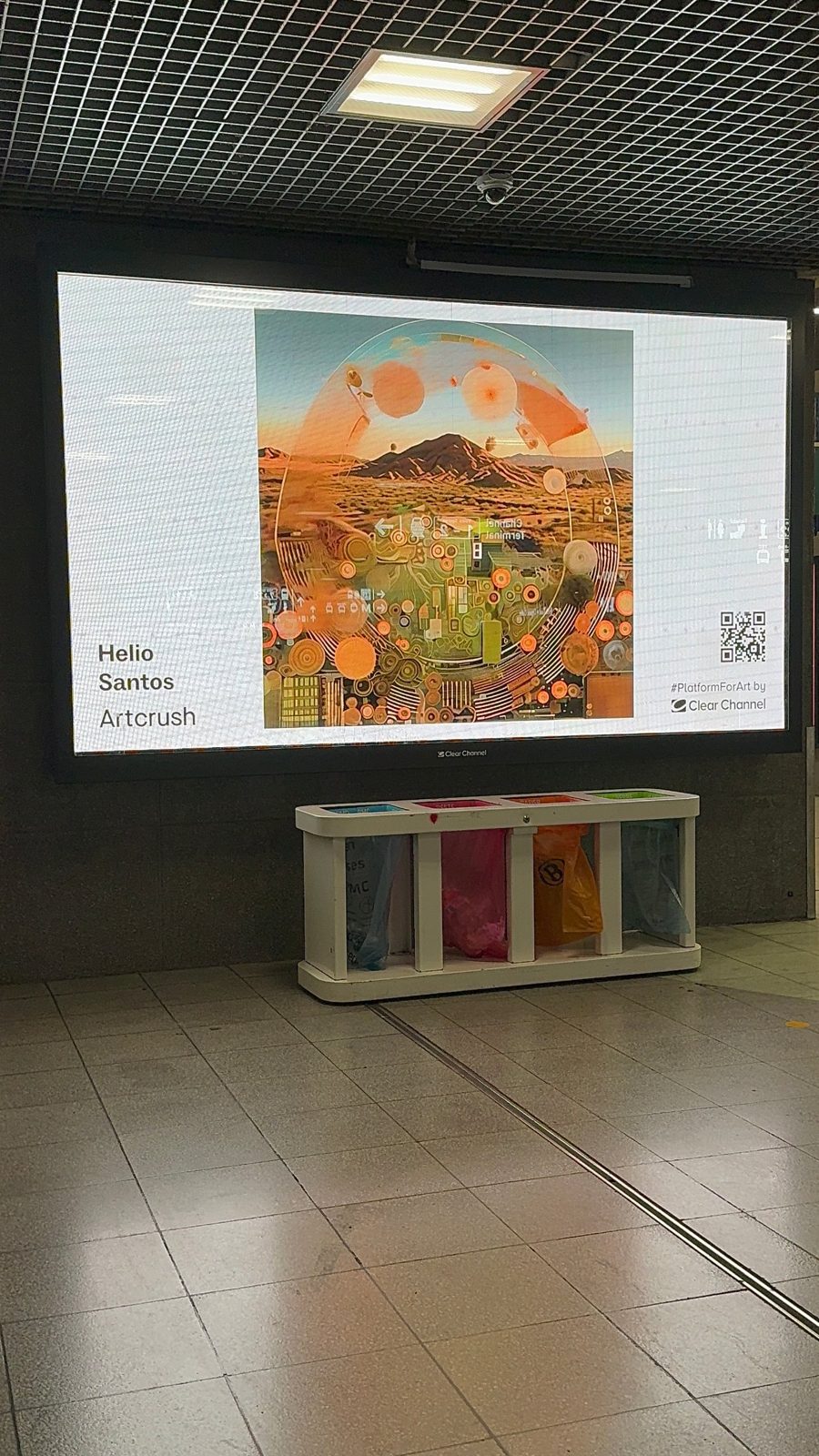 Wide screen in a Brussels station showing a desert landscape with circular forms